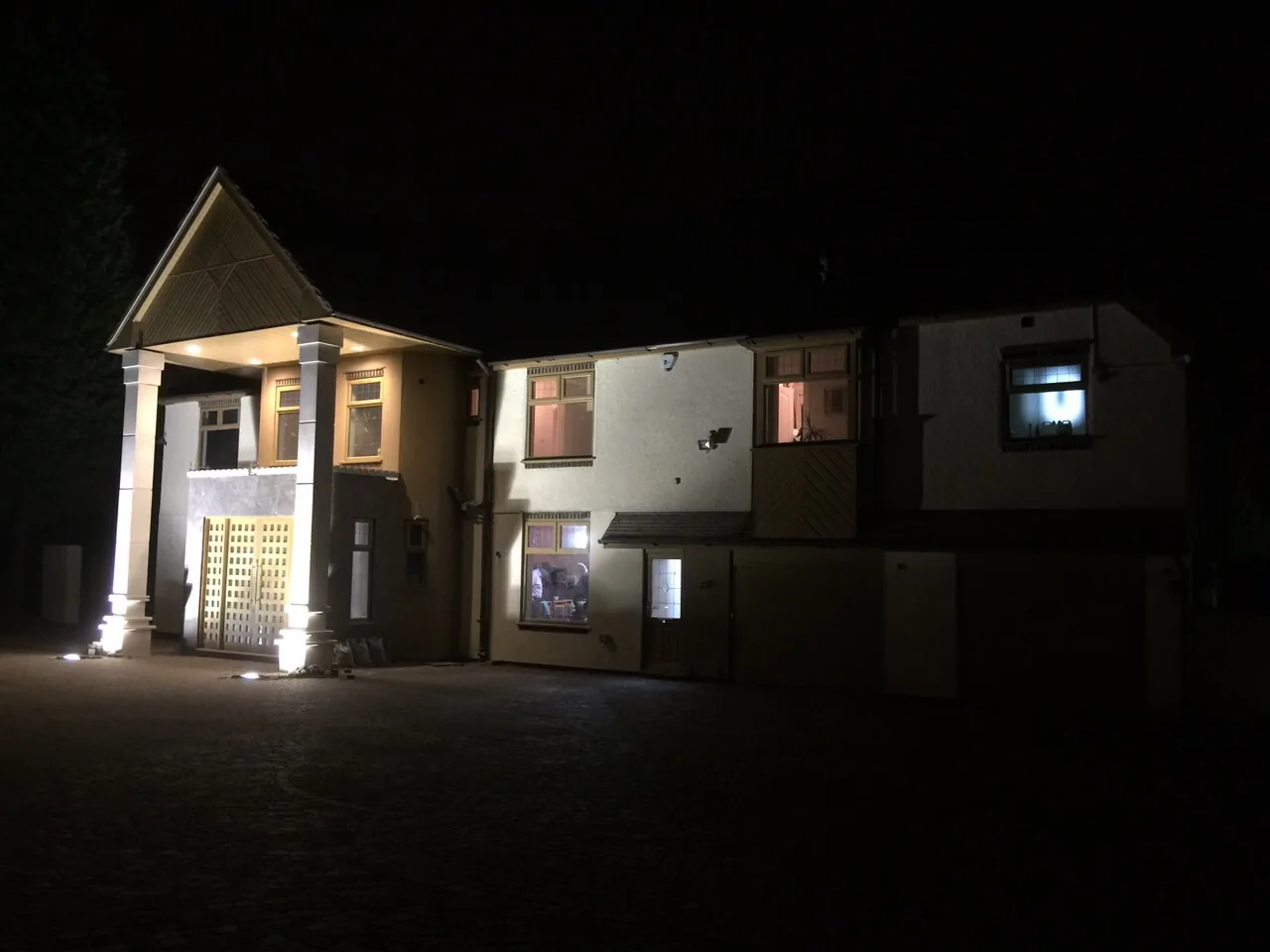 Full house exterior at night showing new silicone render, oak-effect double glazing and driveway lighting scheme, Sunningdale